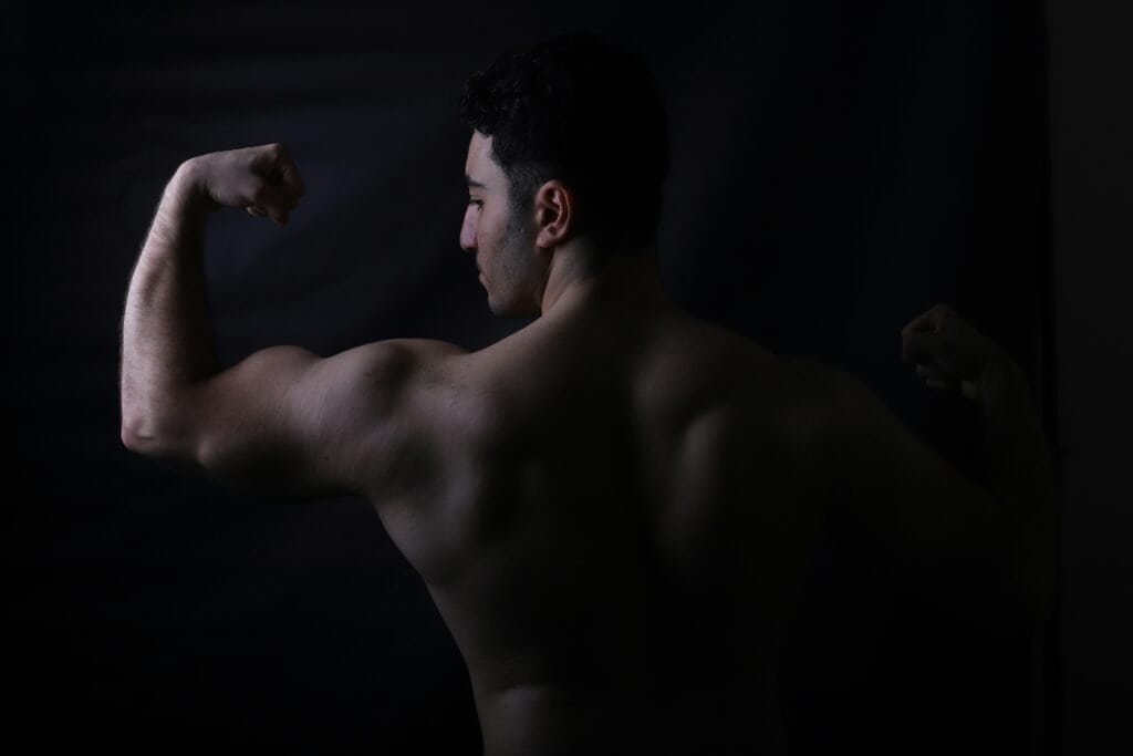 man flexing back and arm muscles to show workout progress over time